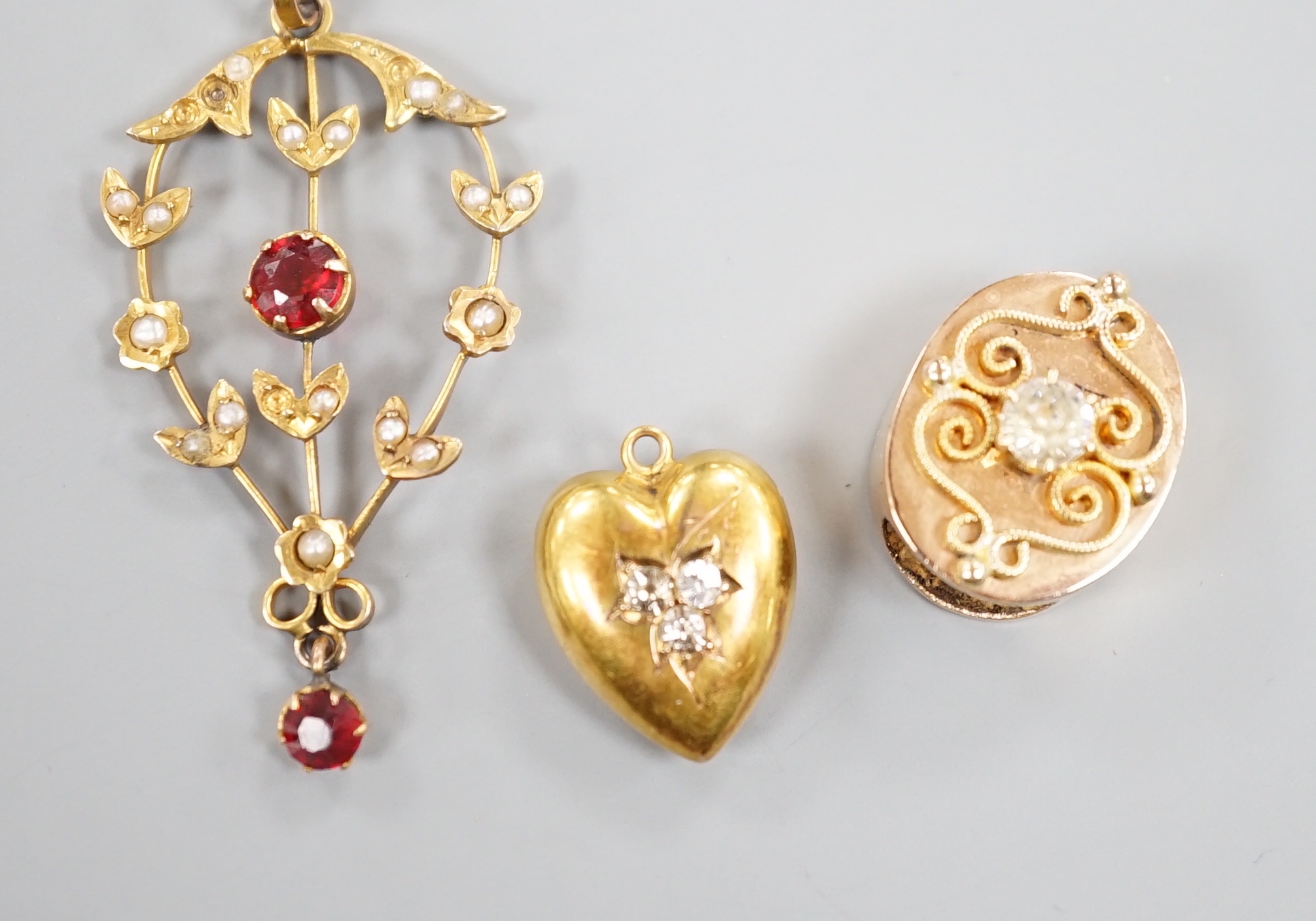 An early 20th century 15ct gold and three stone diamond set heart pendant, 16mm, gross 1.9 grams, an Austro-Hungarian yellow metal and paste set claps and a 9ct, gem and seed pearl set drop pendant, gross 2.6 grams.